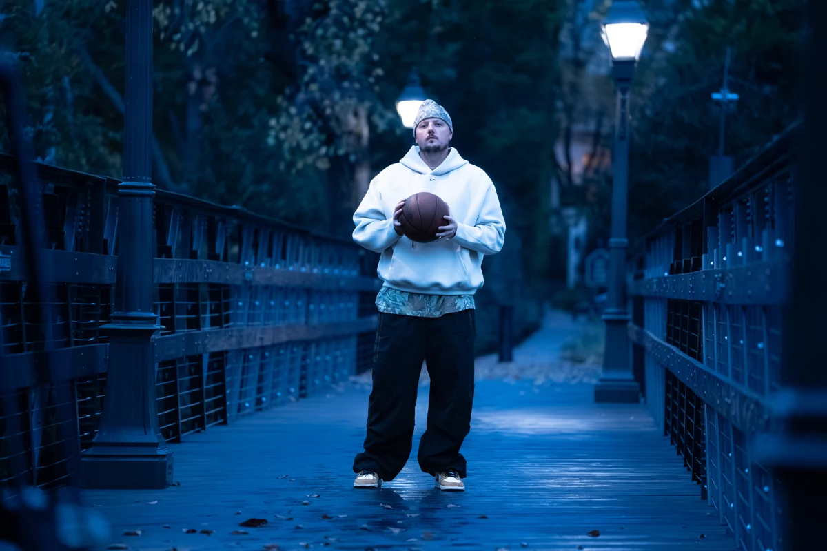 Trey Slate holding a basketball on a tree-lined bridge.
